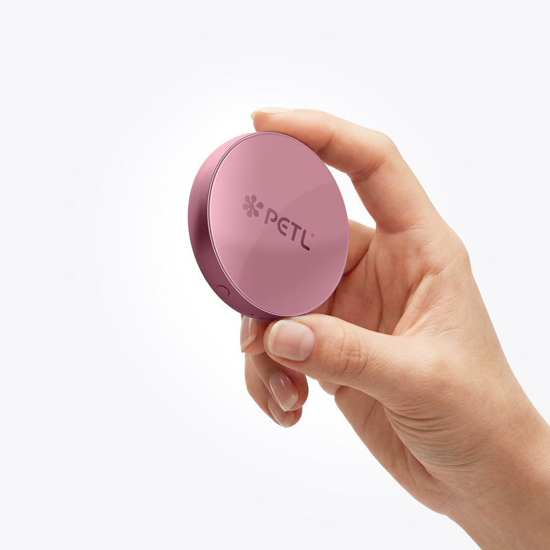 A hand holds a round mauve PETL MagSafe battery pack against a white background.